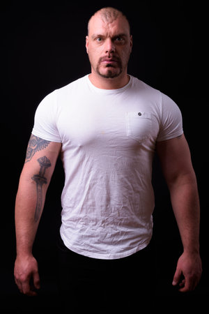 Portrait of muscular bald man against black background