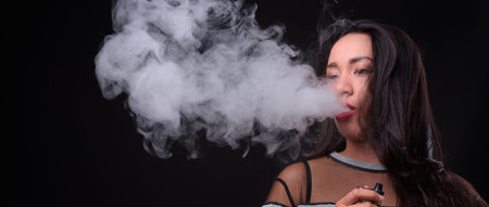Young beautiful Asian woman vaping against black background