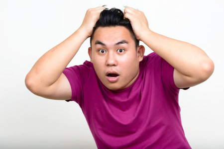 Portrait of young handsome overweight Asian man looking shocked