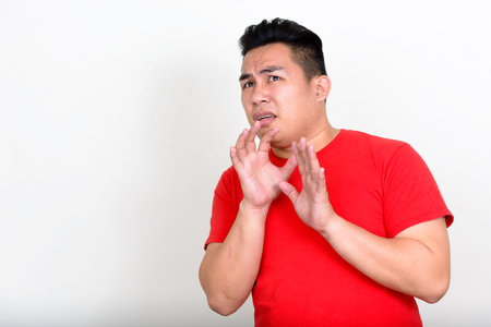 Portrait of stressed young overweight Asian man looking scared