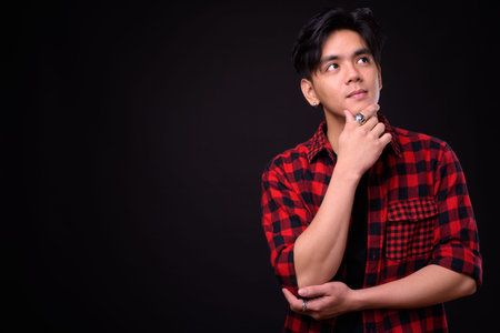 Young handsome Asian hipster man against black background