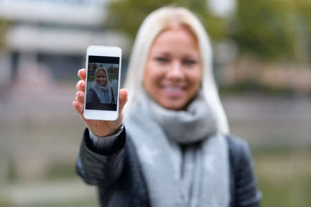 Happy young beautiful blonde woman taking selfie at the park by the riverの写真素材