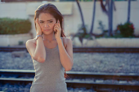 Stressed young Asian woman talking on the phone at the railway stationの写真素材
