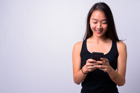 Portrait of happy young beautiful Asian woman using phoneの写真素材