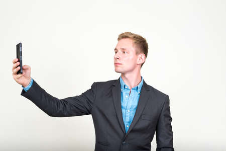 Portrait of young handsome blond businessman in suit taking selfieの写真素材