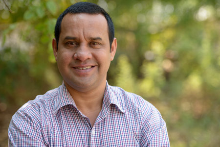 Portrait of happy overweight Indian businessman at the park outdoors
