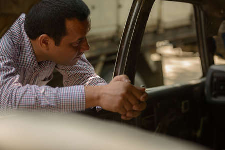 Portrait of overweight Indian businessman with rusty old car outdoorsの写真素材
