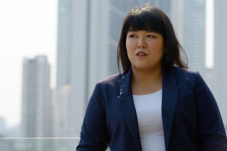 Young beautiful overweight Asian businesswoman against view of the city