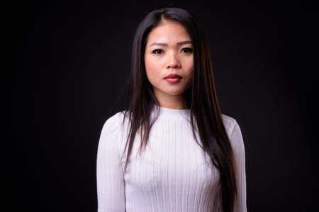 Portrait of young beautiful Asian woman against black background