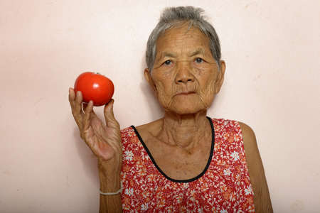 Portrait of senior Asian woman with gray hair holding tomatoの写真素材