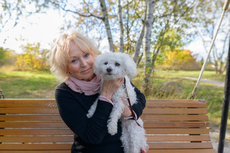 Senior woman holding her pet dog while sitting on wooden bench with natural scenic view of the park
