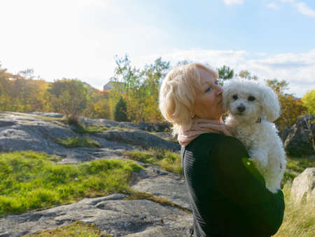 Senior woman thinking while holding dog and standing on boulder in the mountainsの写真素材
