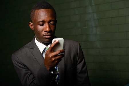 Young African businessman in suit against brick wall