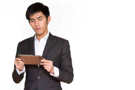 Studio shot of young handsome Asian businessman using digital tablet isolated against white backgroundの写真素材