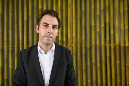Portrait of businessman with brown hair wearing suit against bamboo wall outdoors