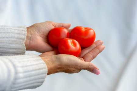 Hands of mature woman holding tomatoes against white linen