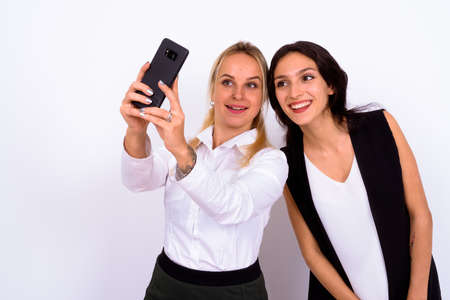 Portrait of two happy young beautiful businesswomen taking selfie togetherの写真素材