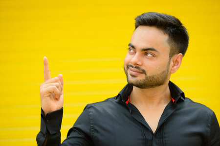 Young handsome bearded Indian businessman against yellow backgroundの写真素材
