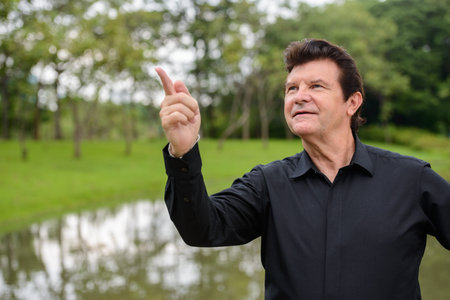 Portrait of happy mature handsome businessman relaxing at the park