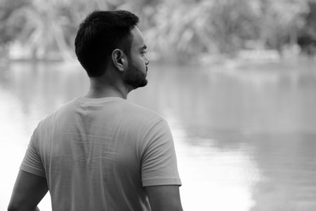Young handsome bearded Indian man at the park in black and whiteの写真素材