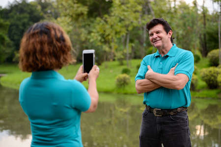 Portrait of mature man and mature Asian woman as multi ethnic married couple together and in love at the park outdoorsの写真素材