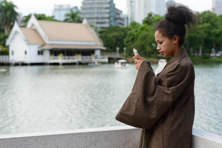 Portrait of young beautiful African woman using phone at the parkの写真素材