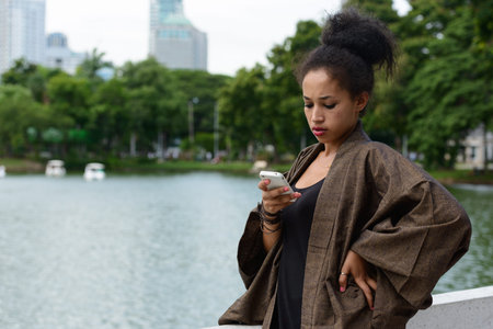 Portrait of young beautiful African woman using phone at the park