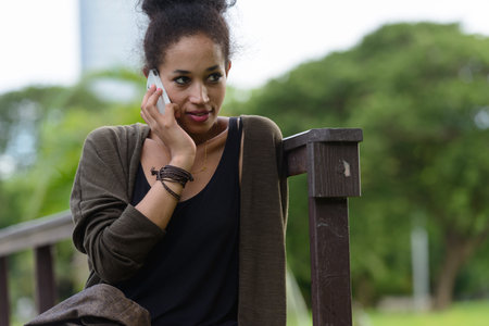 Portrait of young beautiful African woman talking on the phone at the park