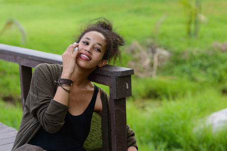Portrait of happy young beautiful African woman talking on the phone at the park
