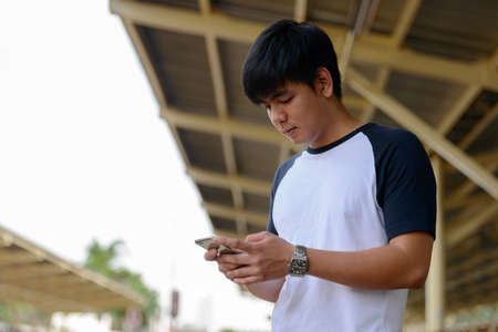 Young handsome Asian tourist man using phone at the railway stationの写真素材
