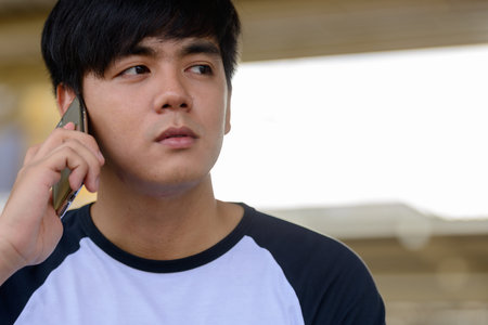 Young handsome Asian tourist man talking on the phone at the railway station