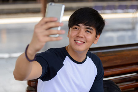 Happy young handsome Asian tourist man taking selfie at the railway station