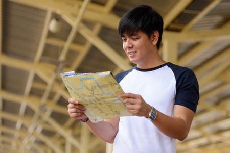 Happy young handsome Asian tourist man at the railway stationの写真素材