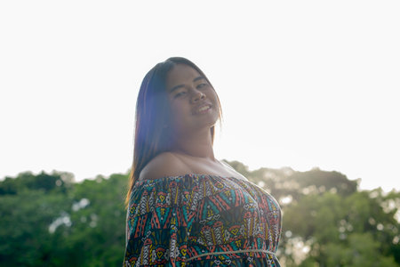 Portrait of happy young overweight Asian woman at the park