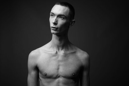 Young handsome androgynous man shirtless against gray background
