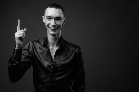 Young handsome androgynous businessman against gray background