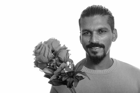 Young happy Indian man holding red roses ready for Valentines day