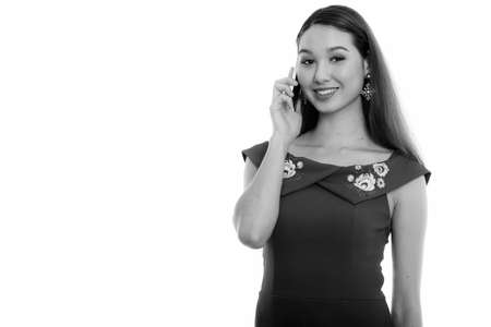 Studio shot of young happy beautiful Asian woman smiling while talking on mobile phoneの写真素材