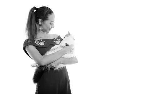 Studio shot of young happy beautiful Asian woman smiling while holding and looking at cute catの写真素材