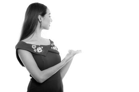 Studio shot of young happy beautiful Asian woman smiling and looking back while showing something on the wallの写真素材