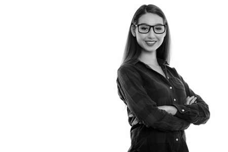 Studio shot of young happy beautiful Asian woman smiling while wearing eyeglasses with arms crossedの写真素材
