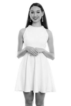 Studio shot of young happy beautiful Asian woman smiling and standing with hands togetherの写真素材