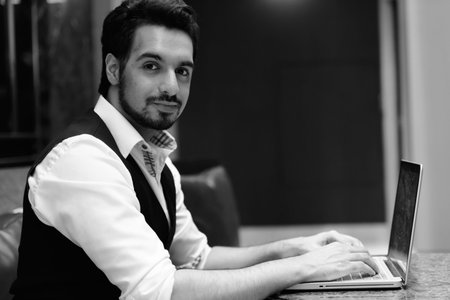Young handsome Indian man using laptop in the lobby of hotel