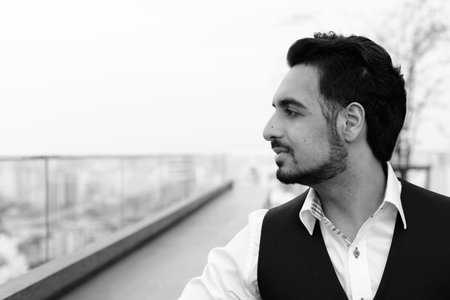 Profile view of young handsome Indian man thinking at rooftop restaurant