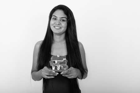 Studio shot of young happy Indian woman smiling while holding house figurine against white backgroundの写真素材