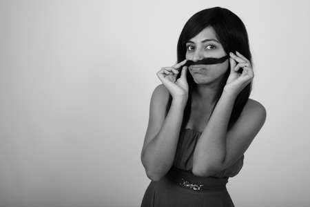 Studio shot of young Persian woman using hair as mustache while wearing dress against gray backgroundの写真素材