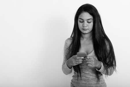 Studio shot of young Indian woman using mobile phone against white backgroundの写真素材