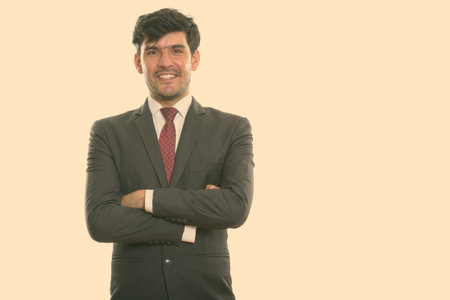 Studio shot of young happy Persian businessman smiling with arms crossed