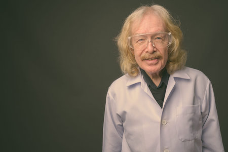 Senior man doctor with mustache wearing protective glasses against gray backgroundの写真素材