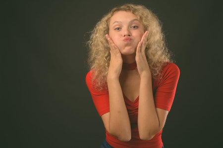 Young beautiful woman with blond curly hair against gray background